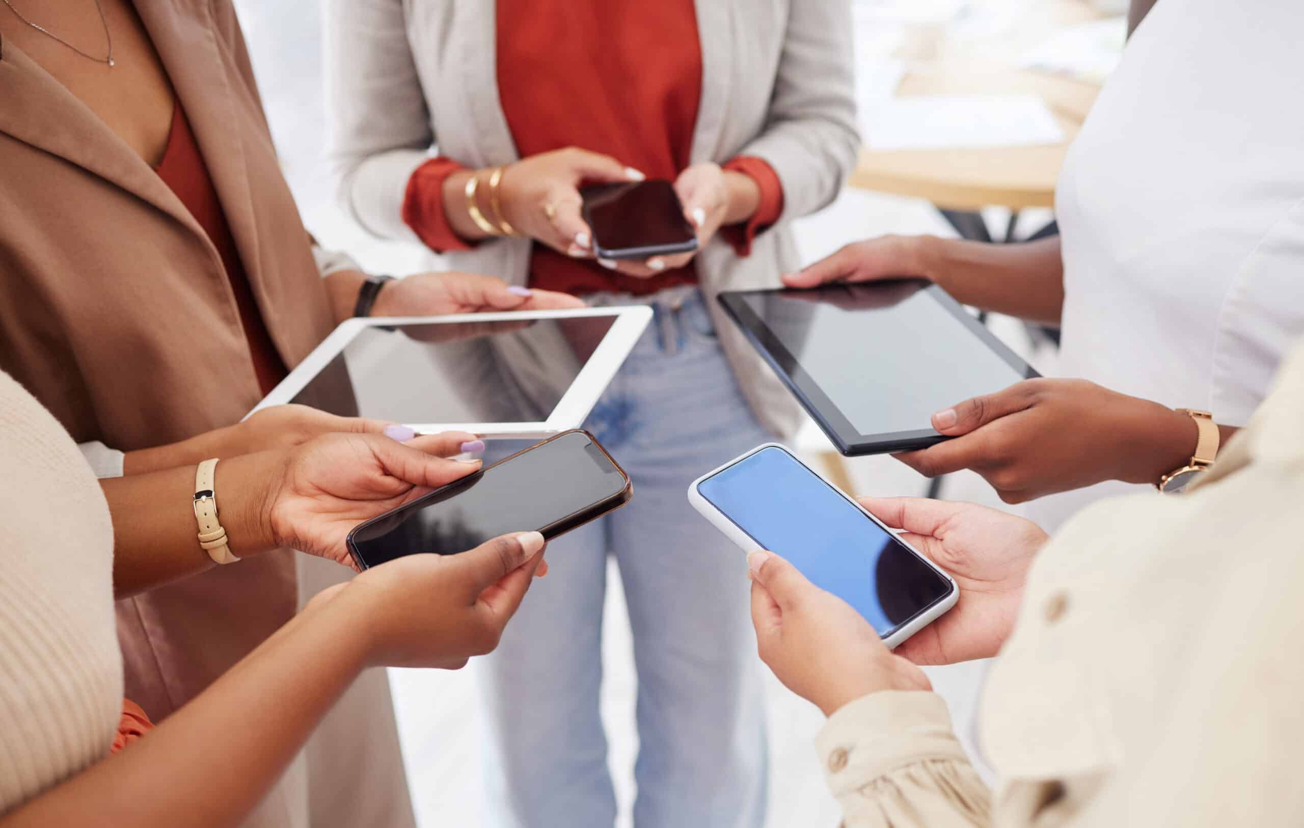 Diverse group of unknown ambitious businesswomen huddled together and using cellphones in the middl.